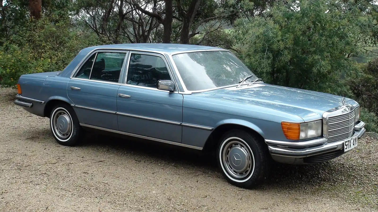Light blue Mercedes-Benz W116 S-Class saloon photographed from the front three-quarter angle in a gravel driveway