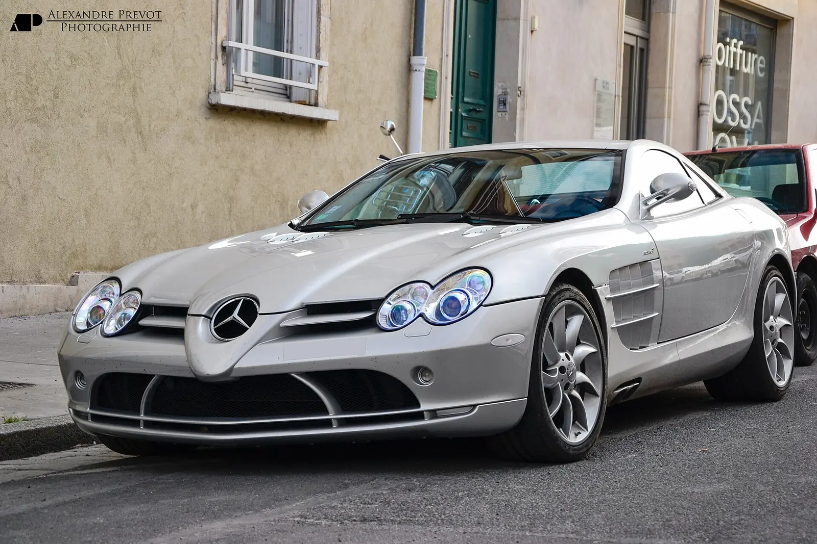 Silver Mercedes-Benz SLR McLaren coupe photographed from the front three-quarter angle, parked on a street beside a building