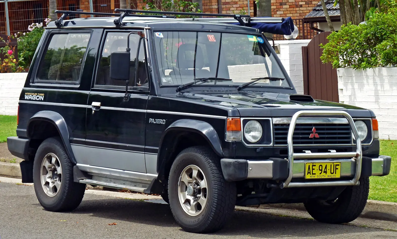 Black first-generation Mitsubishi Pajero three-door hardtop with a chrome bull bar, photographed from the front three-quarter angle on a residential street