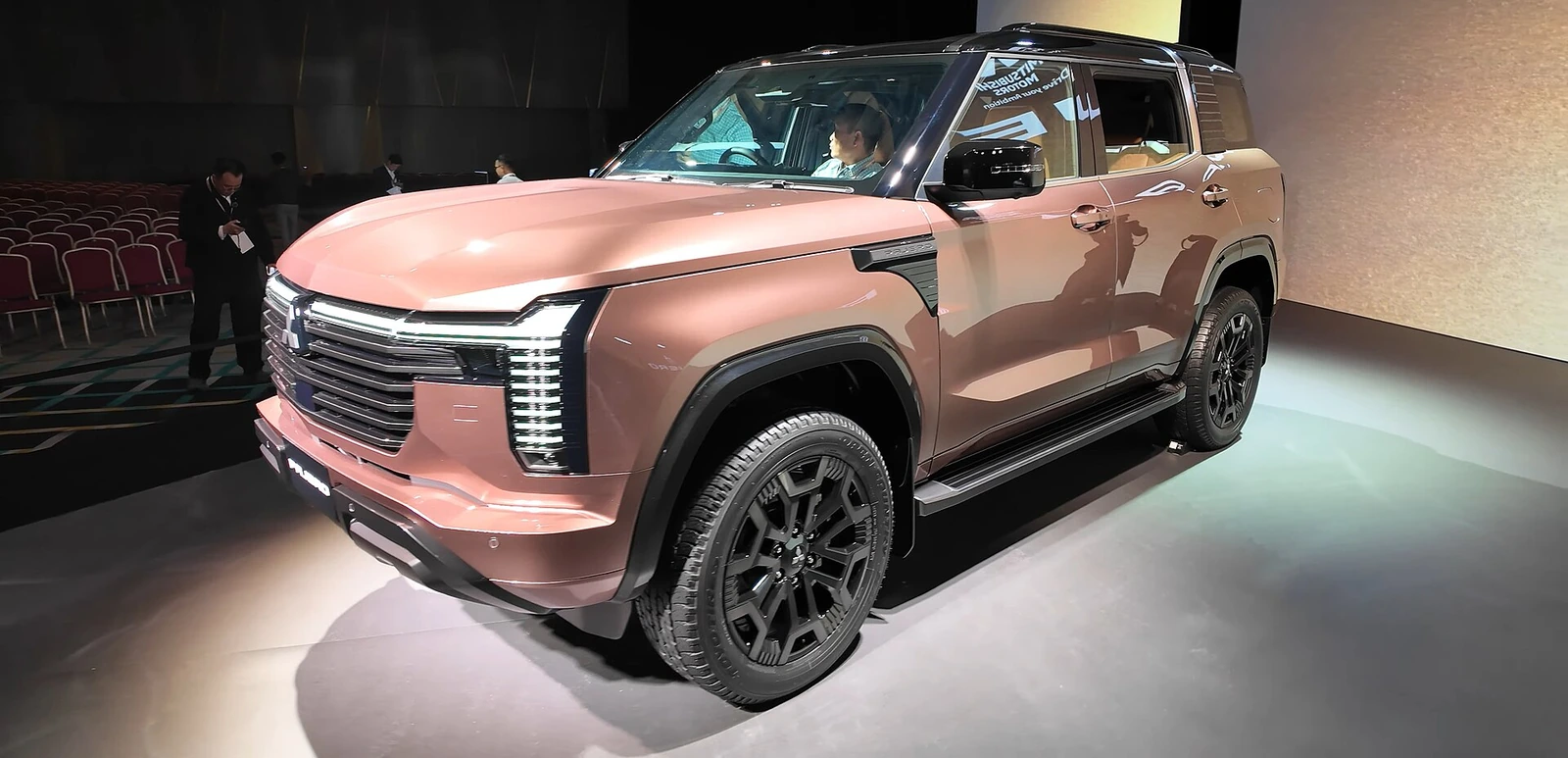 Copper-coloured fifth-generation Mitsubishi Pajero photographed from the front three-quarter angle at its Tokyo launch event, showing its T-shaped LED daytime running lights