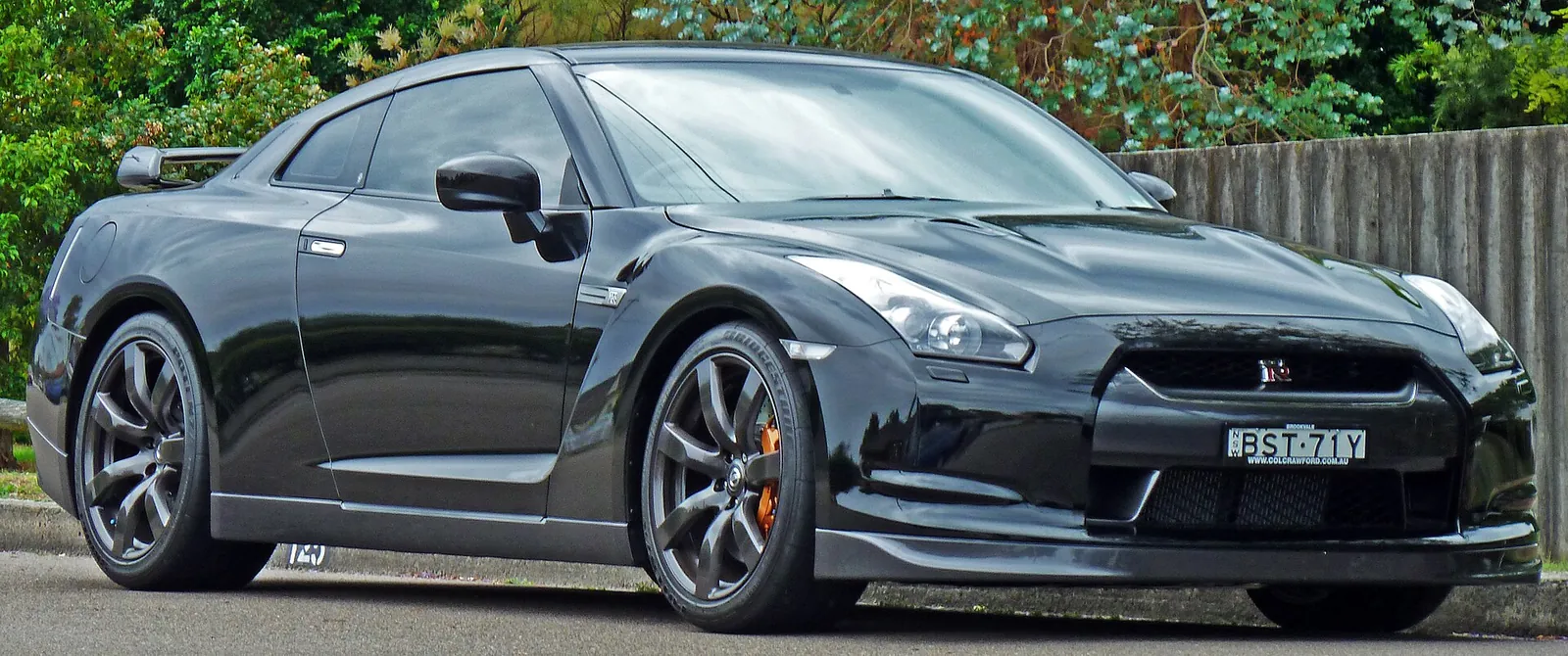 Black pre-facelift Nissan GT-R (R35) photographed from the front three-quarter angle, showing its four round tail-light heritage cues up front and sharply creased bodywork