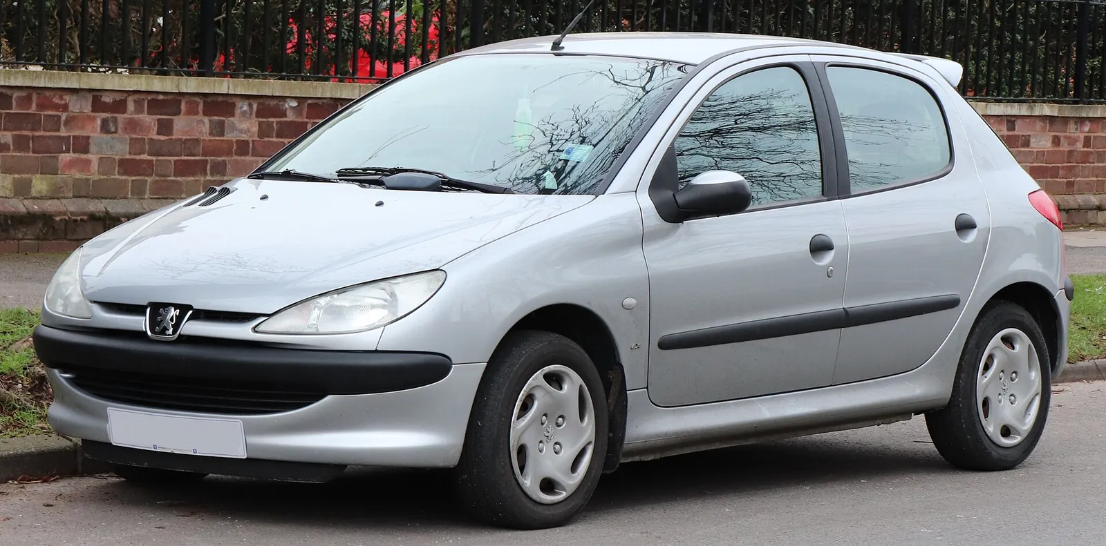 Silver Peugeot 206 5-door hatchback photographed from the front three-quarter angle, parked beside a brick wall