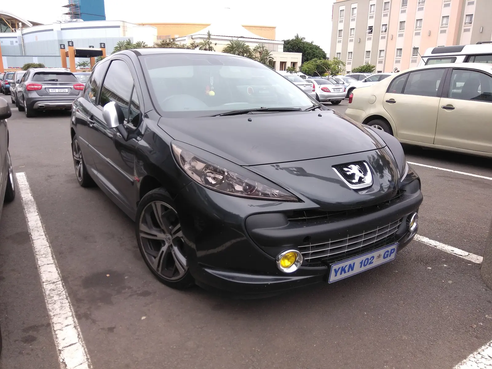 Black Peugeot 207 GTi hot hatch photographed from the front three-quarter angle in a car park, with yellow fog lamps and alloy wheels