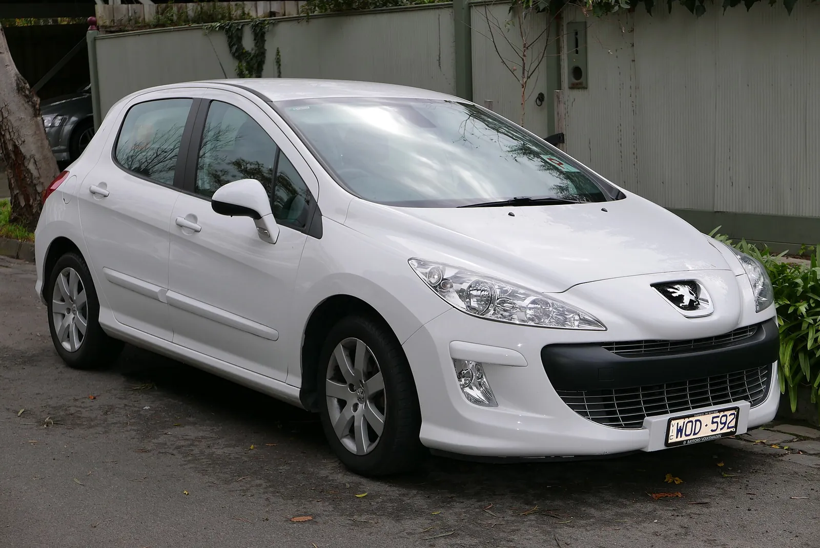White first-generation Peugeot 308 hatchback photographed from the front three-quarter angle on a residential street