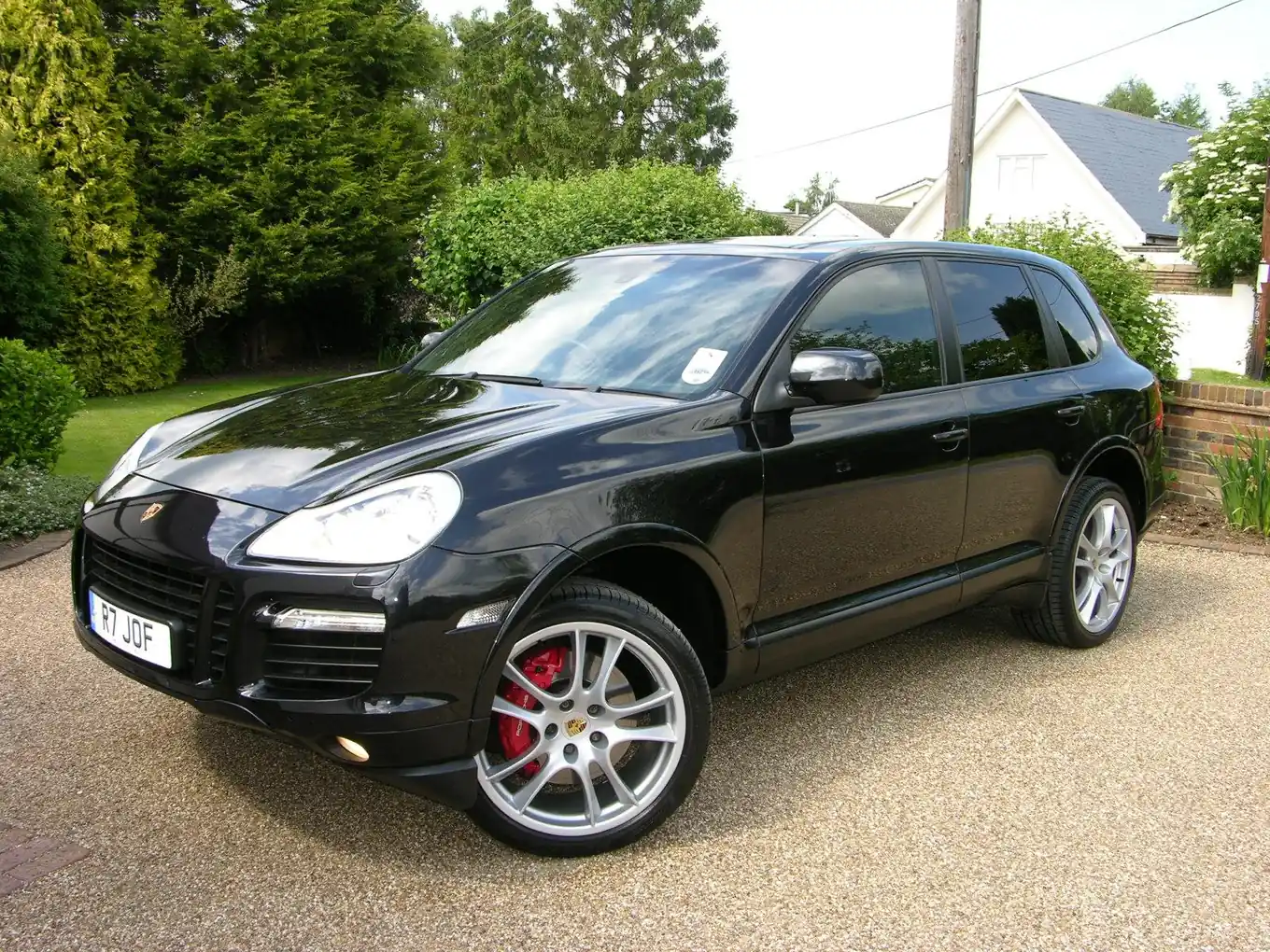 Black first-generation Porsche Cayenne Turbo SUV photographed from the front three-quarter angle on a gravel driveway, with red brake calipers visible