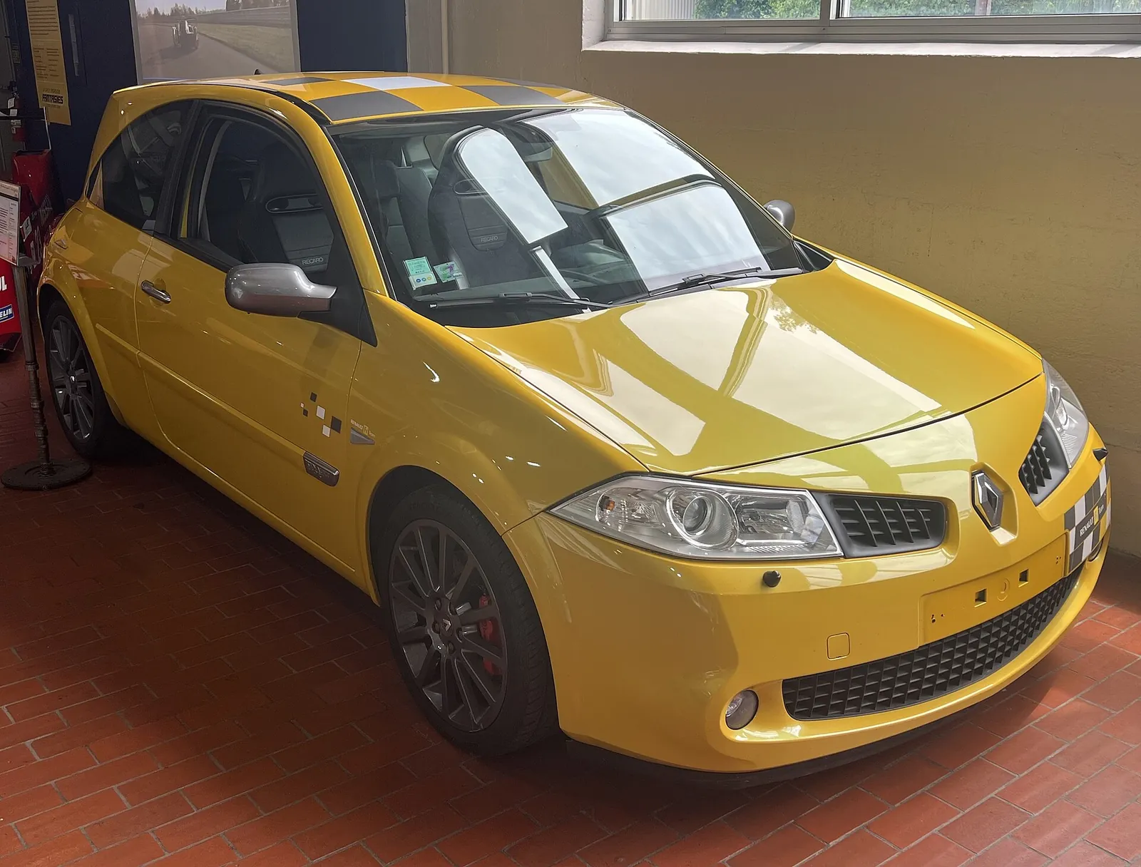 Yellow Renault Mégane R26 Renault Sport hot hatch photographed from the front three-quarter angle in a museum, with black checkerboard roof graphics