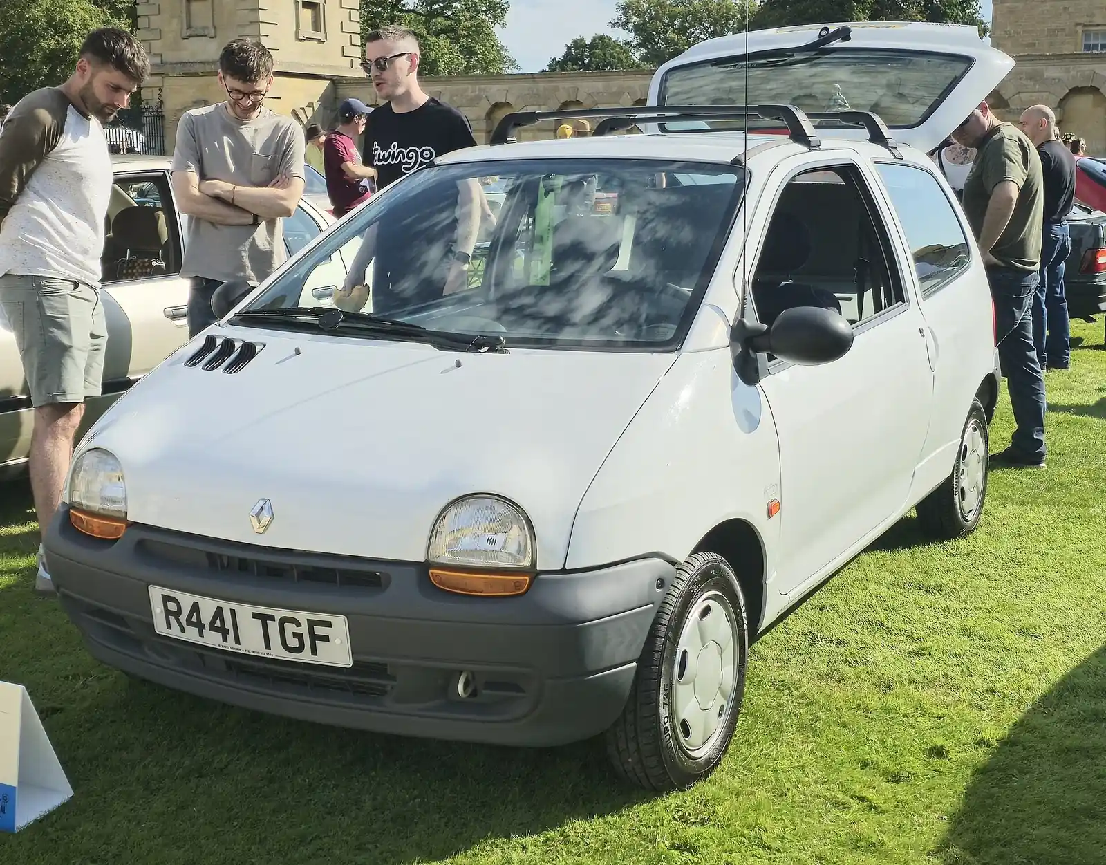 White three-door original Renault Twingo photographed from the front three-quarter angle at an outdoor car show, with its tailgate open