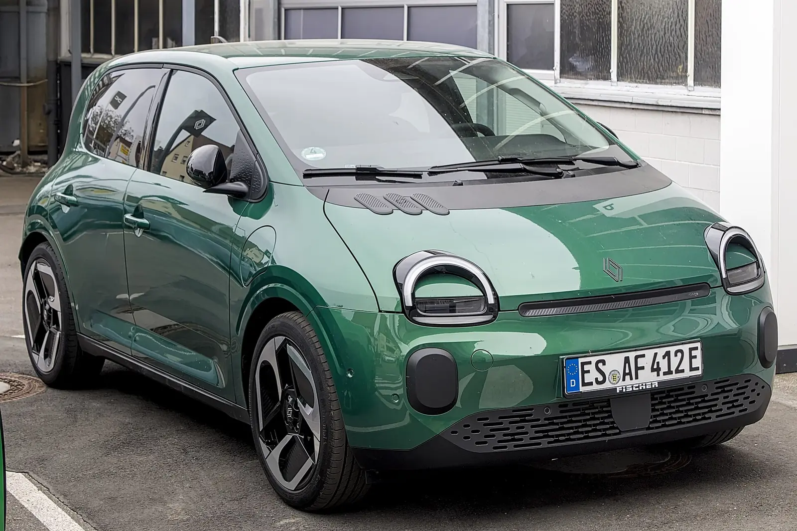 Green Renault Twingo E-Tech electric city car photographed from the front three-quarter angle, showing its rounded headlights and single-box silhouette