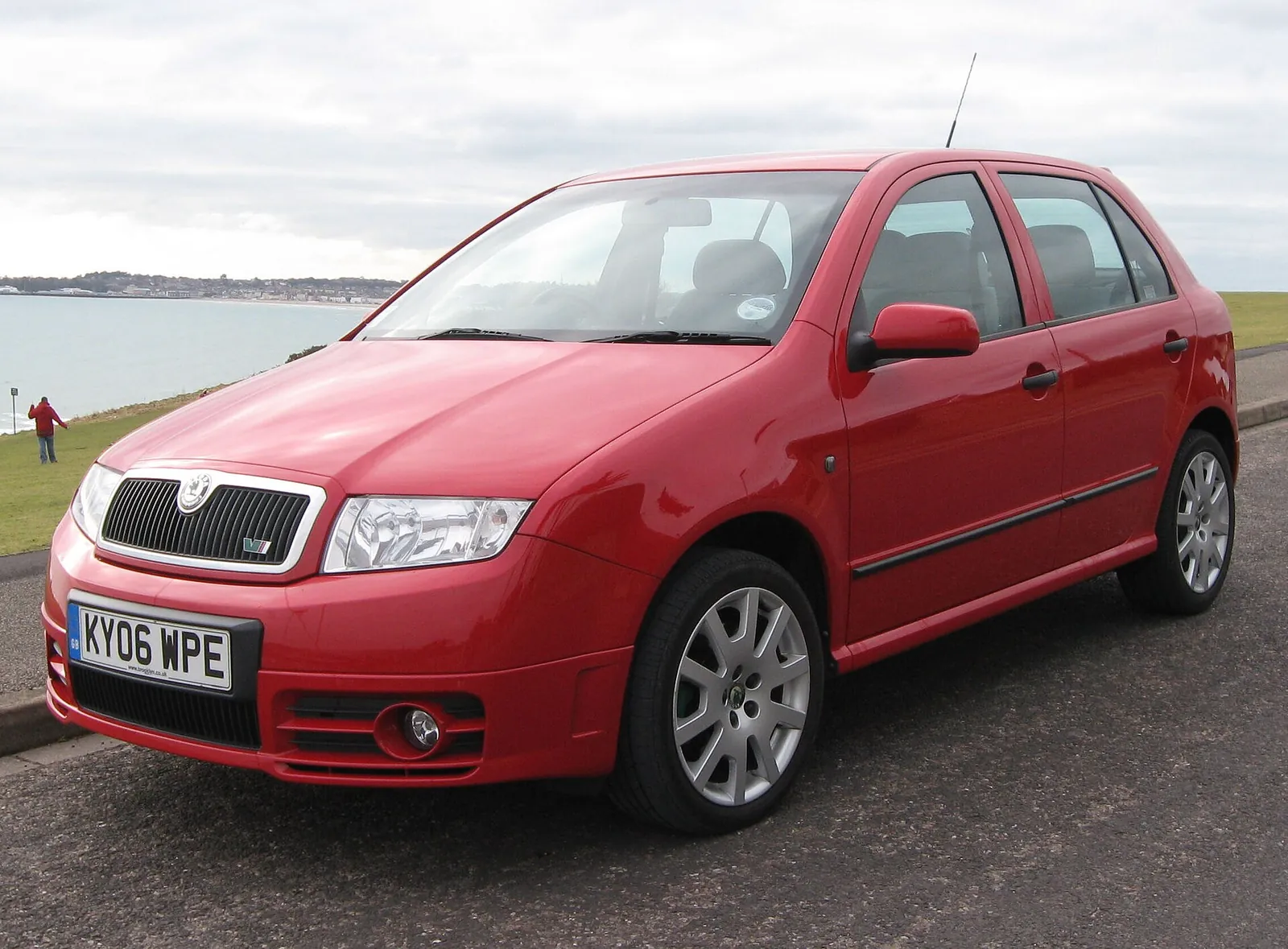 Red first-generation Skoda Fabia vRS hatchback photographed from the front three-quarter angle beside a coastal road