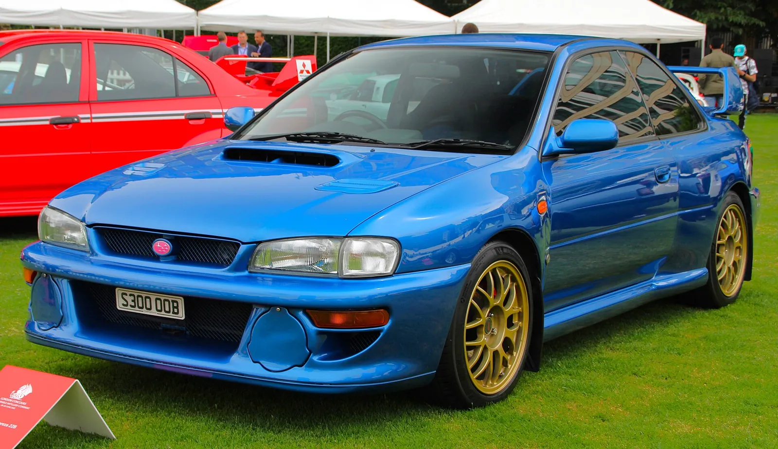 Blue Subaru Impreza 22B STi photographed from the front three-quarter angle at a car show, showing its widened fenders and gold BBS wheels