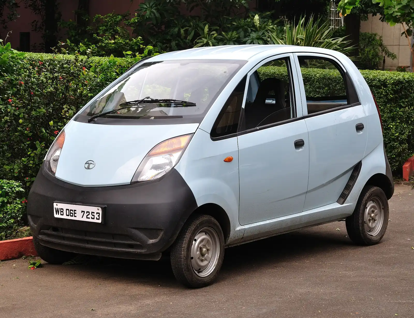 Pale blue Tata Nano photographed from the front three-quarter angle, showing its rounded one-box body, single driver's-side mirror and steel wheels