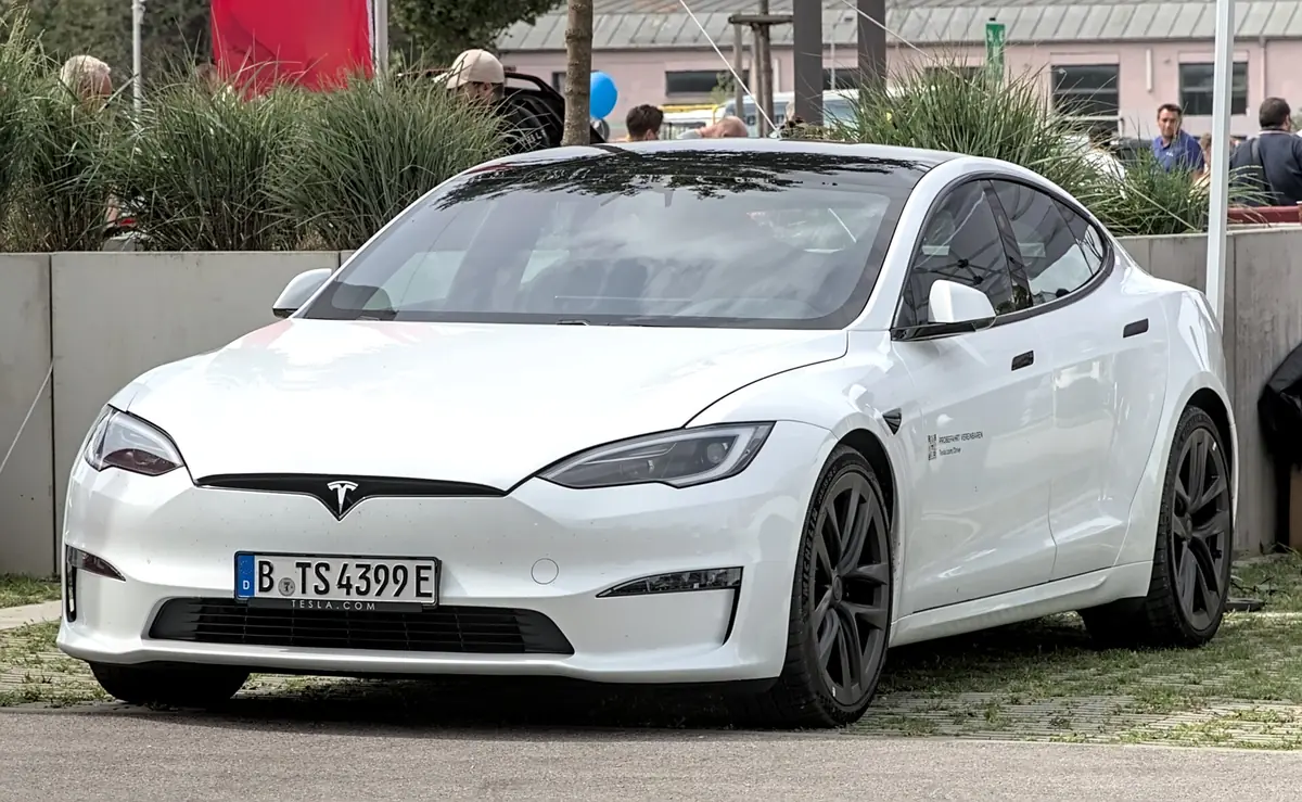 White Tesla Model S photographed from the front three-quarter angle at an outdoor event, with a smooth closed front fascia and no visible grille
