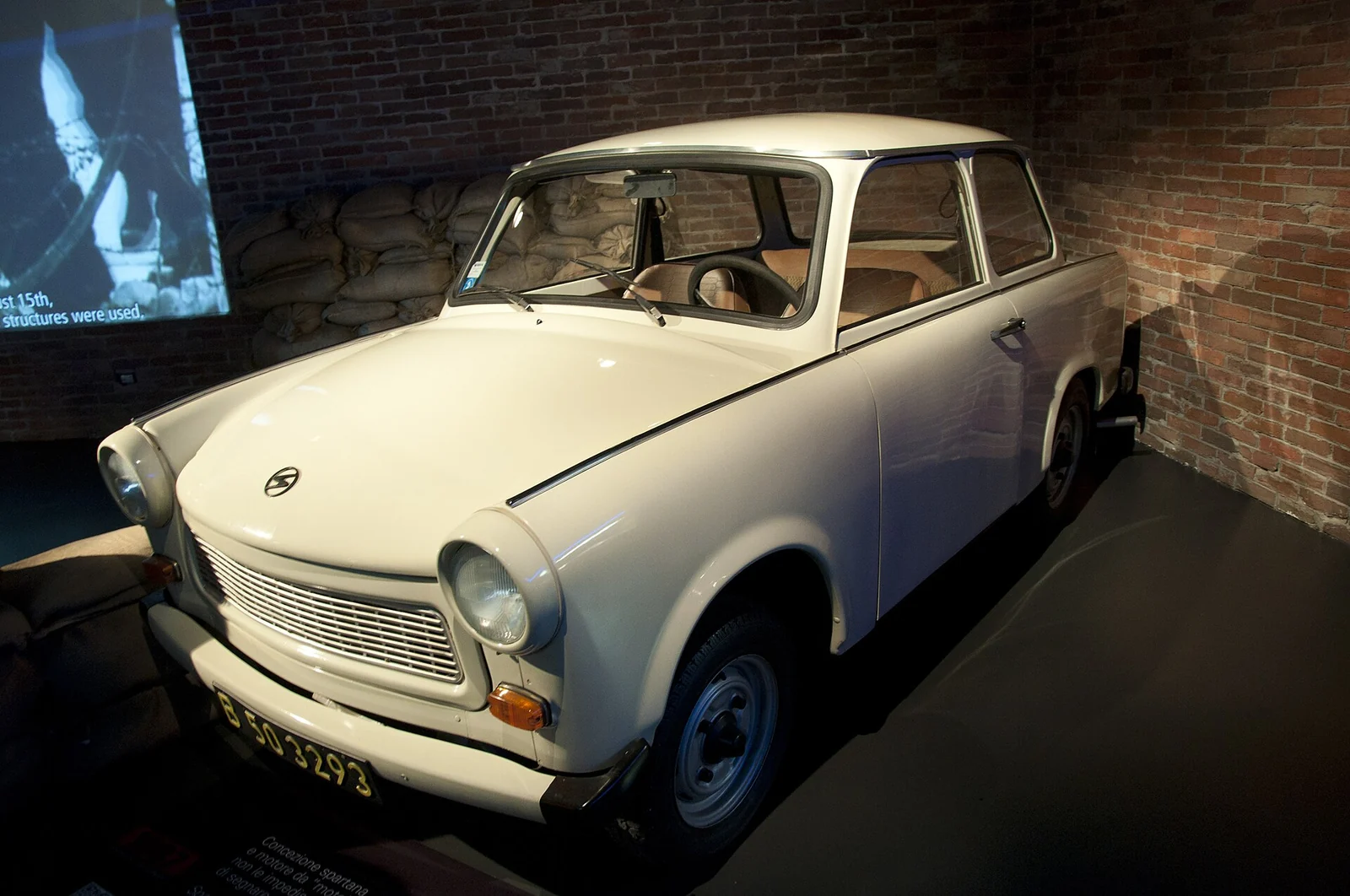 Blue Trabant 601 saloon photographed from the front three-quarter angle in a museum, showing its slab-sided body and rectangular grille