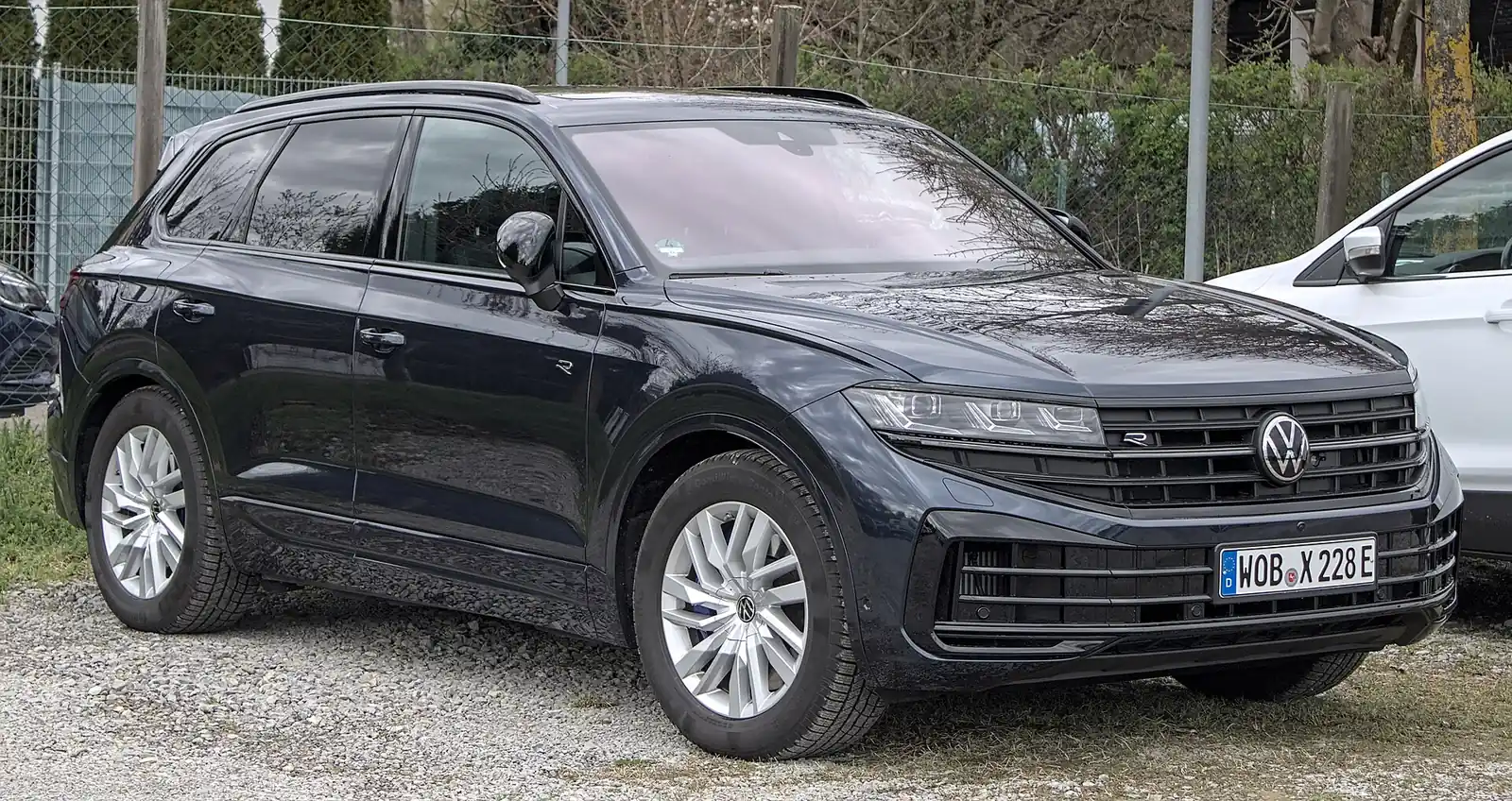 Dark blue-grey third-generation Volkswagen Touareg R photographed from the front three-quarter angle, showing its illuminated grille strip and R badging