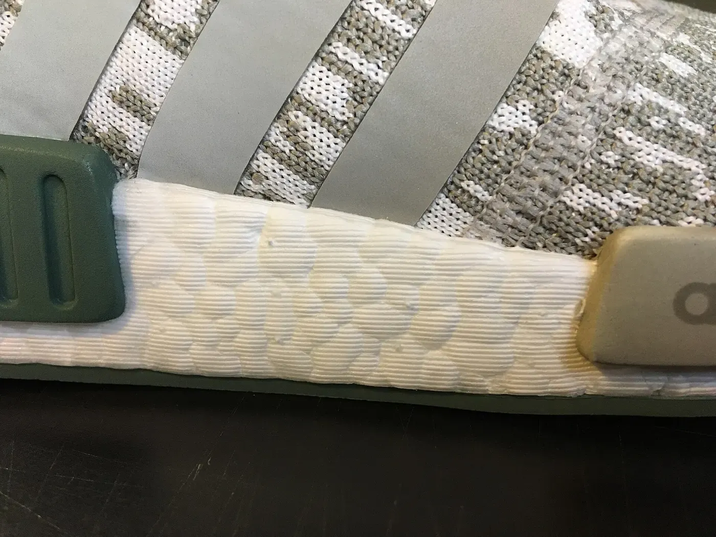 Close-up of a white, textured foam midsole strip made of small fused granules, set into the side of a grey and white knit running shoe.
