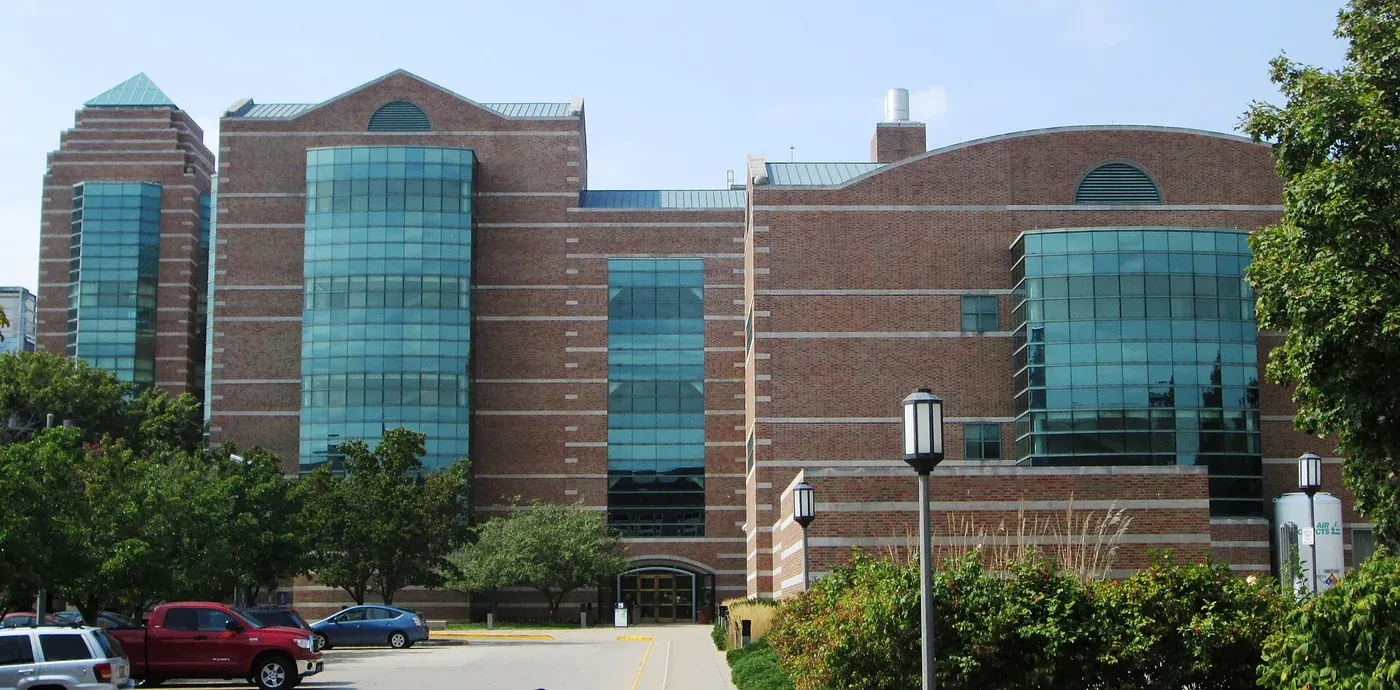 A large brick and glass laboratory building with curved glazed bays, seen from a car park and tree-lined path.