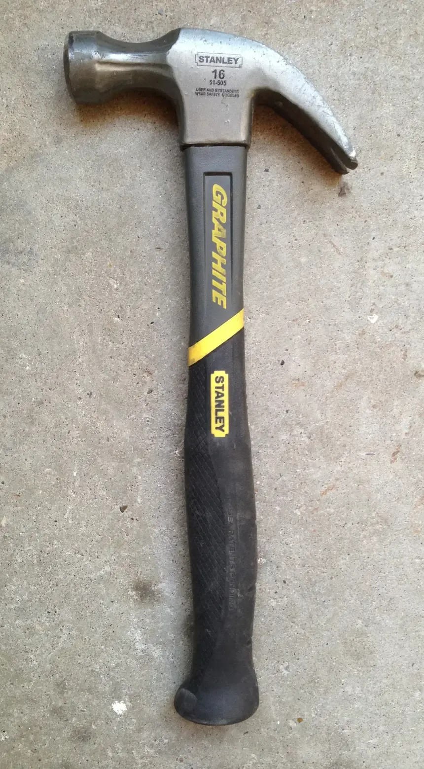 A steel-headed claw hammer with a black and yellow rubber-gripped handle, resting on a concrete floor.
