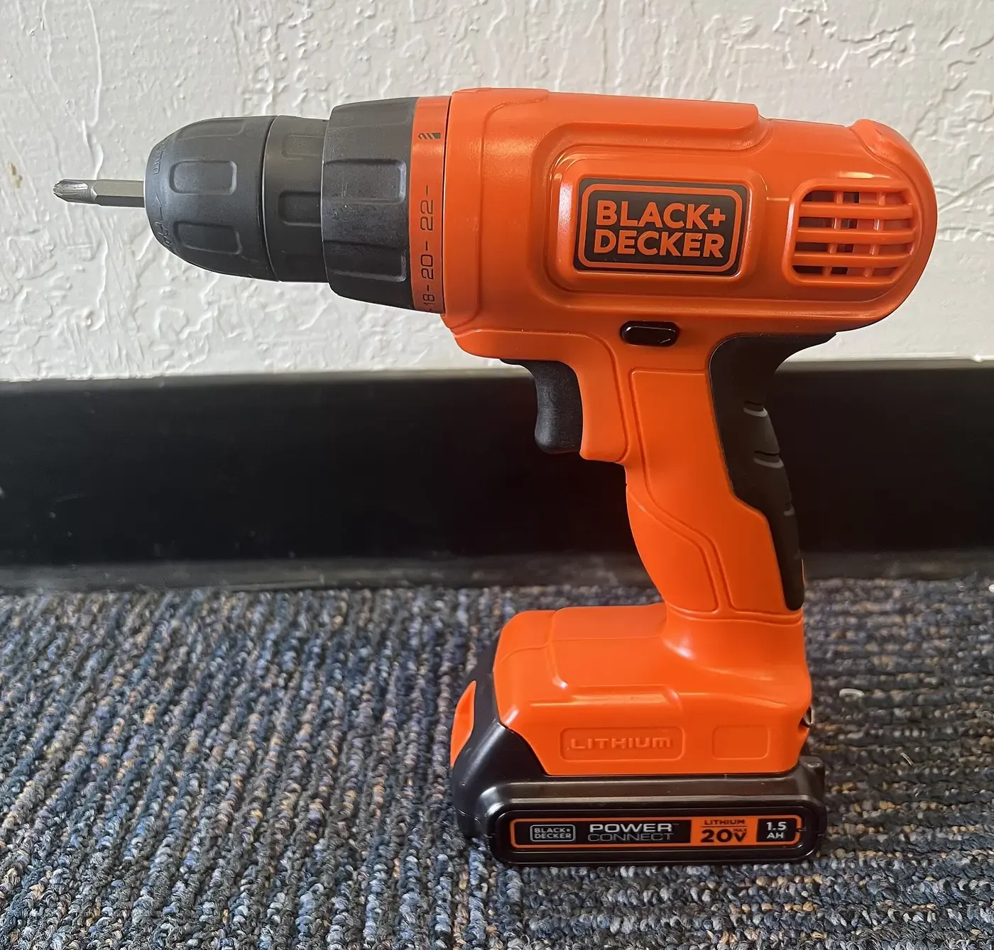 An orange and black cordless power drill standing upright on its battery pack, showing a textured black rubberized grip panel set into the orange handle.
