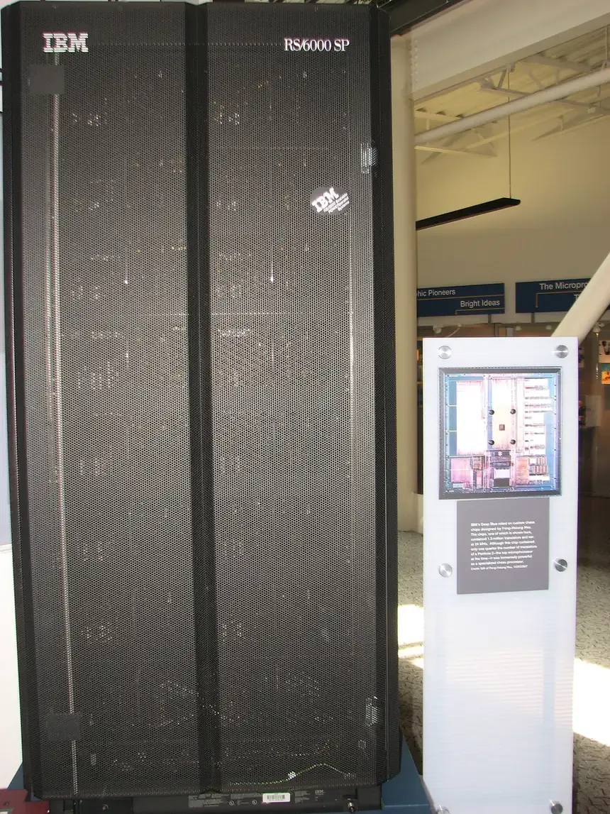A tall black IBM RS/6000 SP server cabinet on display in a museum, beside a wall placard showing one of Deep Blue's custom chess chips and descriptive text.