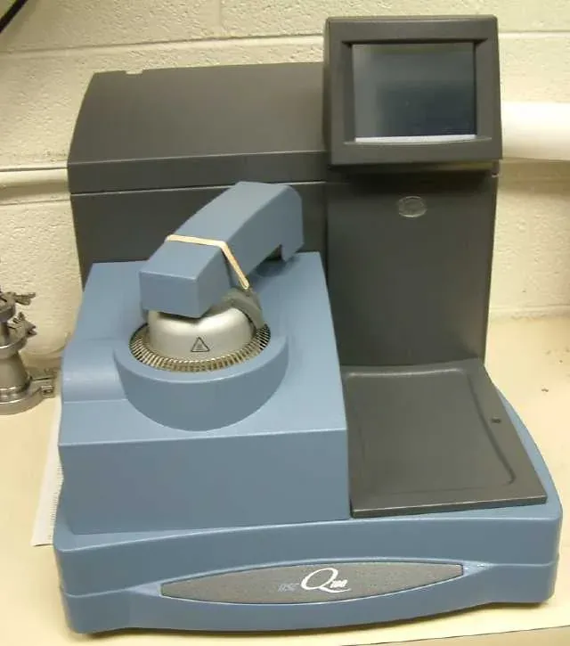 A grey benchtop differential scanning calorimeter with a small sample chamber and an attached touchscreen control panel, on a laboratory countertop.