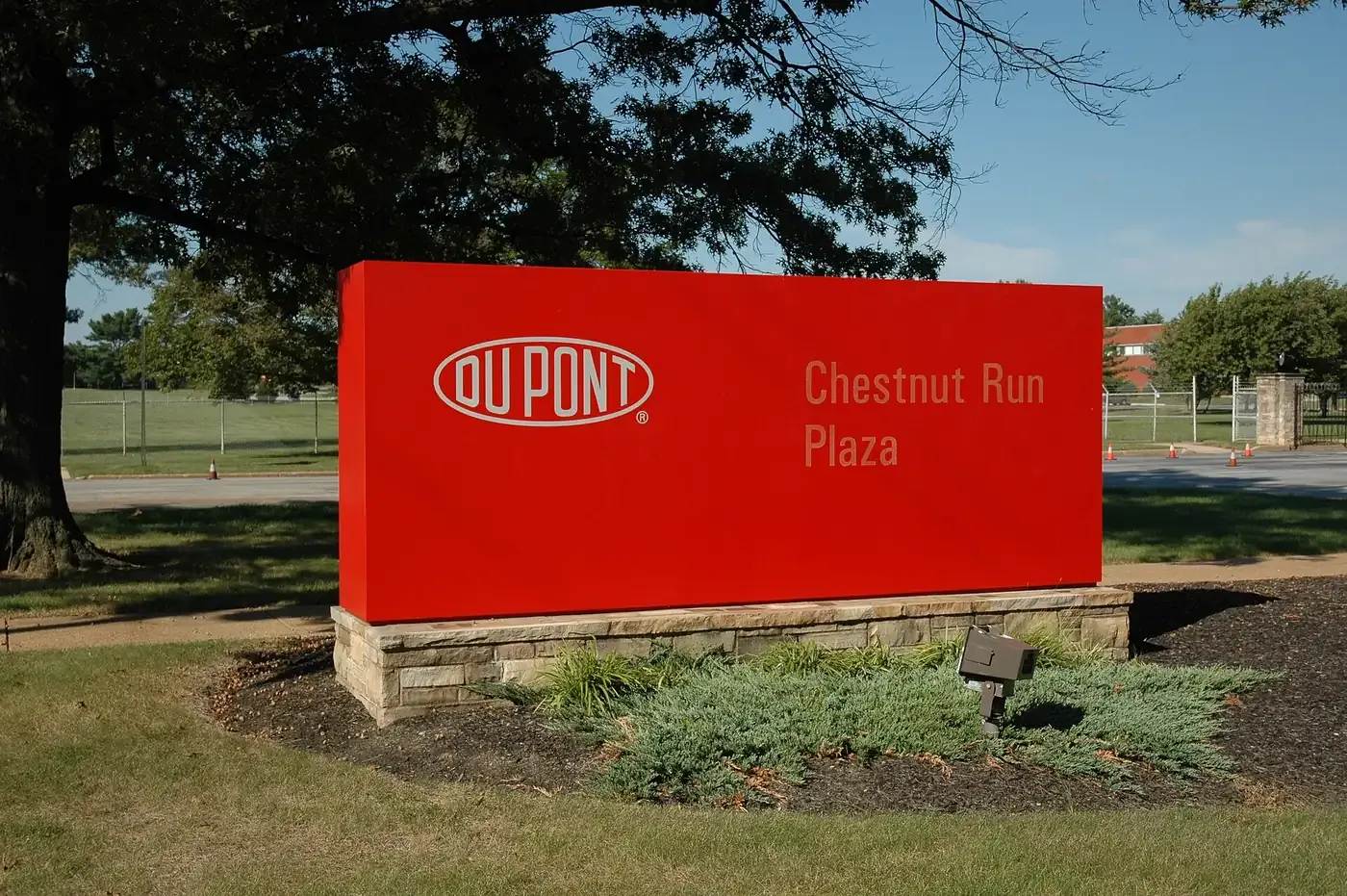 A large red sign reading DU PONT Chestnut Run Plaza on a stone base, in front of a wooded corporate research campus.