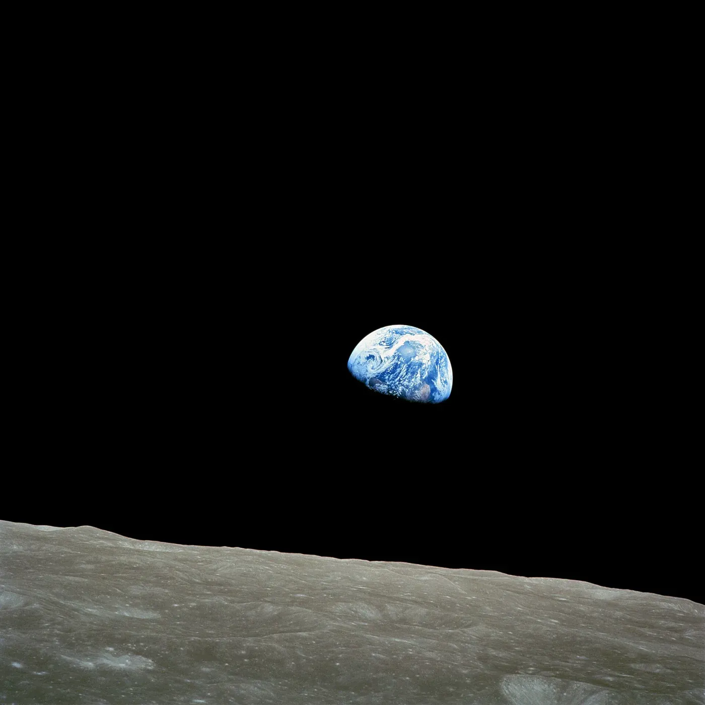 The Earth as a small blue and white sphere, half in shadow, hanging above a grey, cratered lunar horizon against black space.