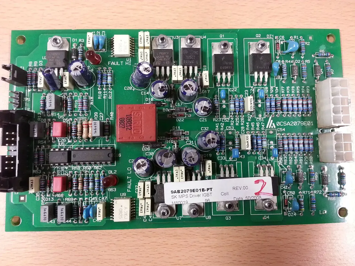 A green printed circuit board densely populated with electronic components, resistors, capacitors and connectors, mounted on a wooden surface.