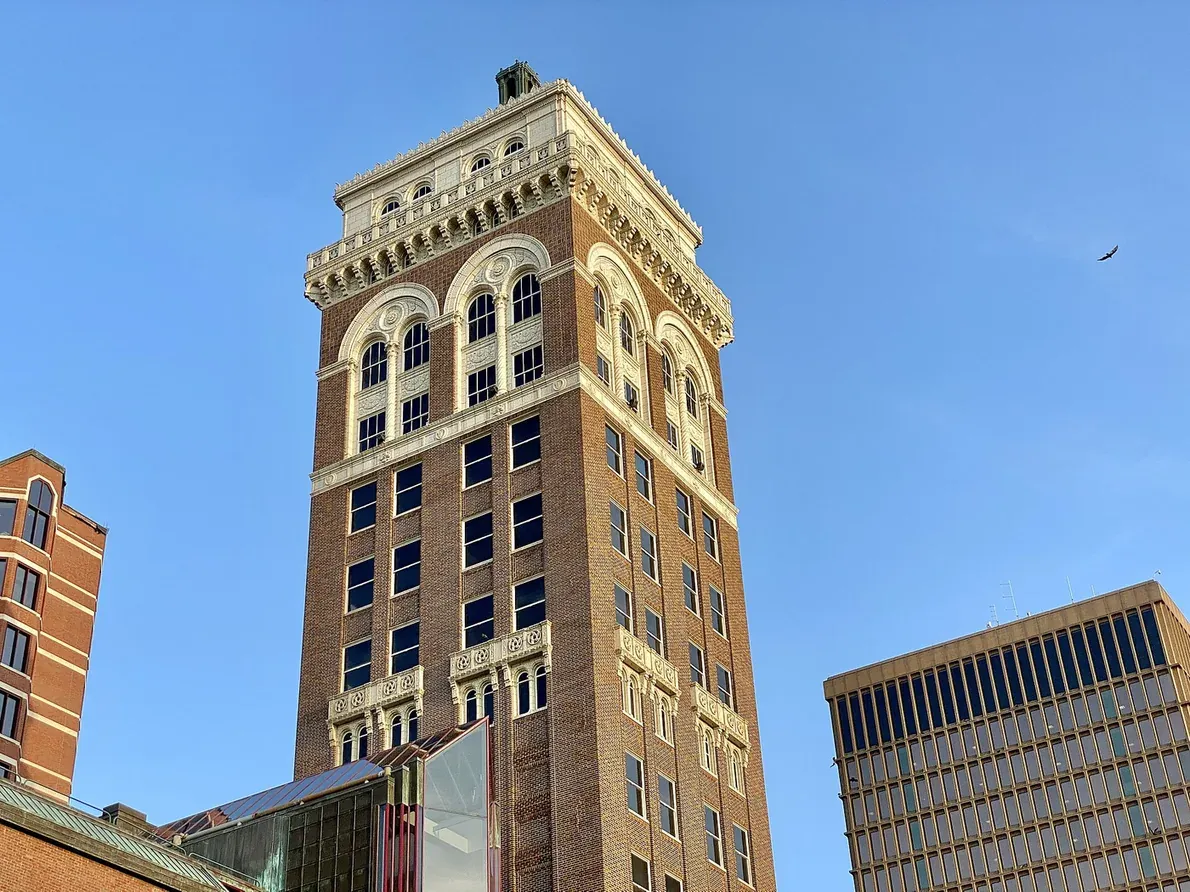 A tall early-twentieth-century brick and terracotta office tower with arched upper-floor windows, photographed from street level against a clear blue sky.