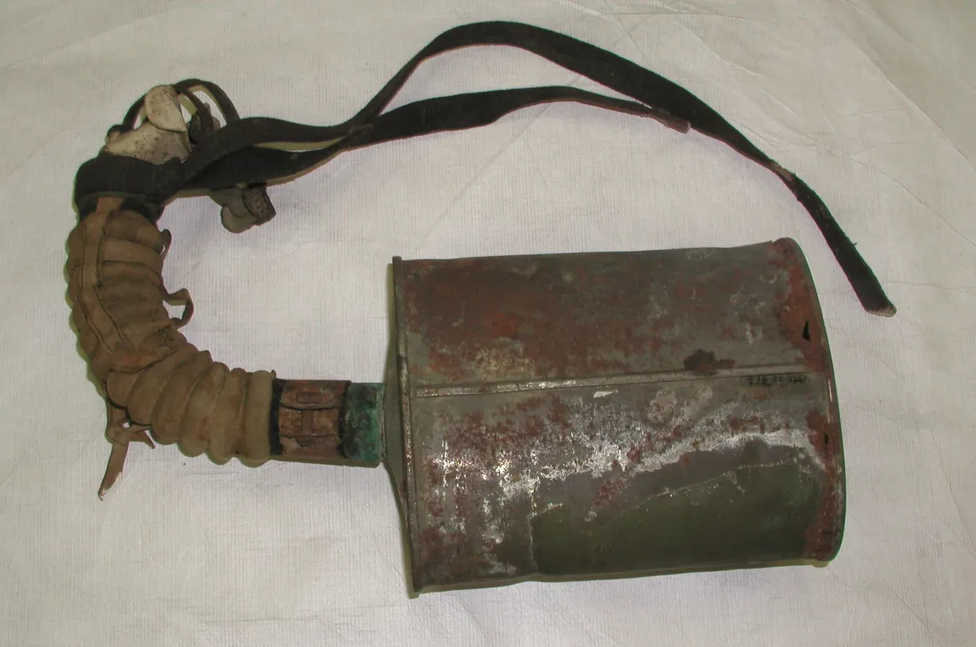 A corroded metal filter canister attached by a corrugated rubber hose to a leather and fabric head harness, laid out on a plain cloth background.