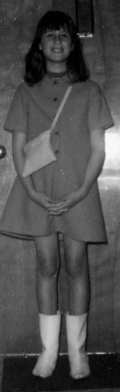 A black-and-white snapshot of a girl in a short shift dress and a shoulder bag, standing indoors and wearing pale knee-high go-go boots.