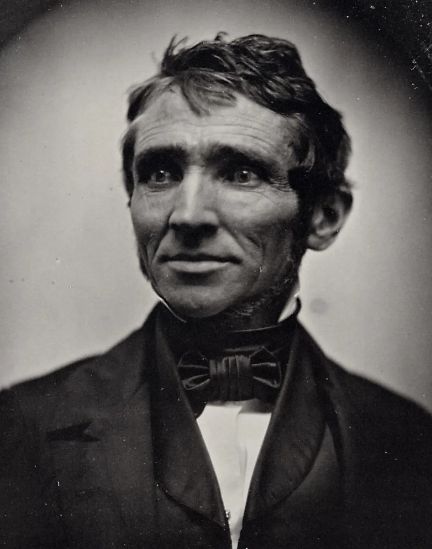 A sepia-toned daguerreotype-style portrait of a middle-aged man with tousled dark hair and a bow tie, looking slightly off-camera.