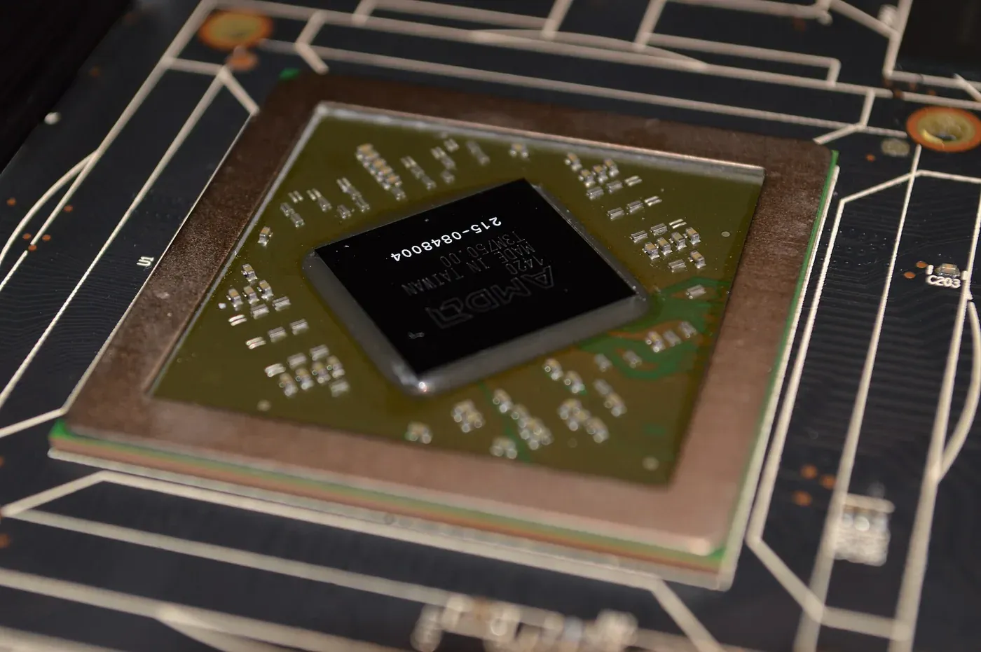 A close-up photograph of a graphics processing unit chip on a green circuit board, its black ceramic package etched with a manufacturer's logo and serial number, surrounded by smaller surface-mounted components.
