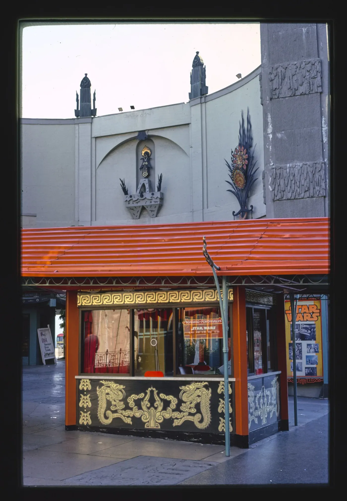 Color photograph of the ornate ticket booth outside Grauman's Chinese Theatre in 1977, its window displaying a hand-lettered 'Star Wars' screening schedule and a poster.