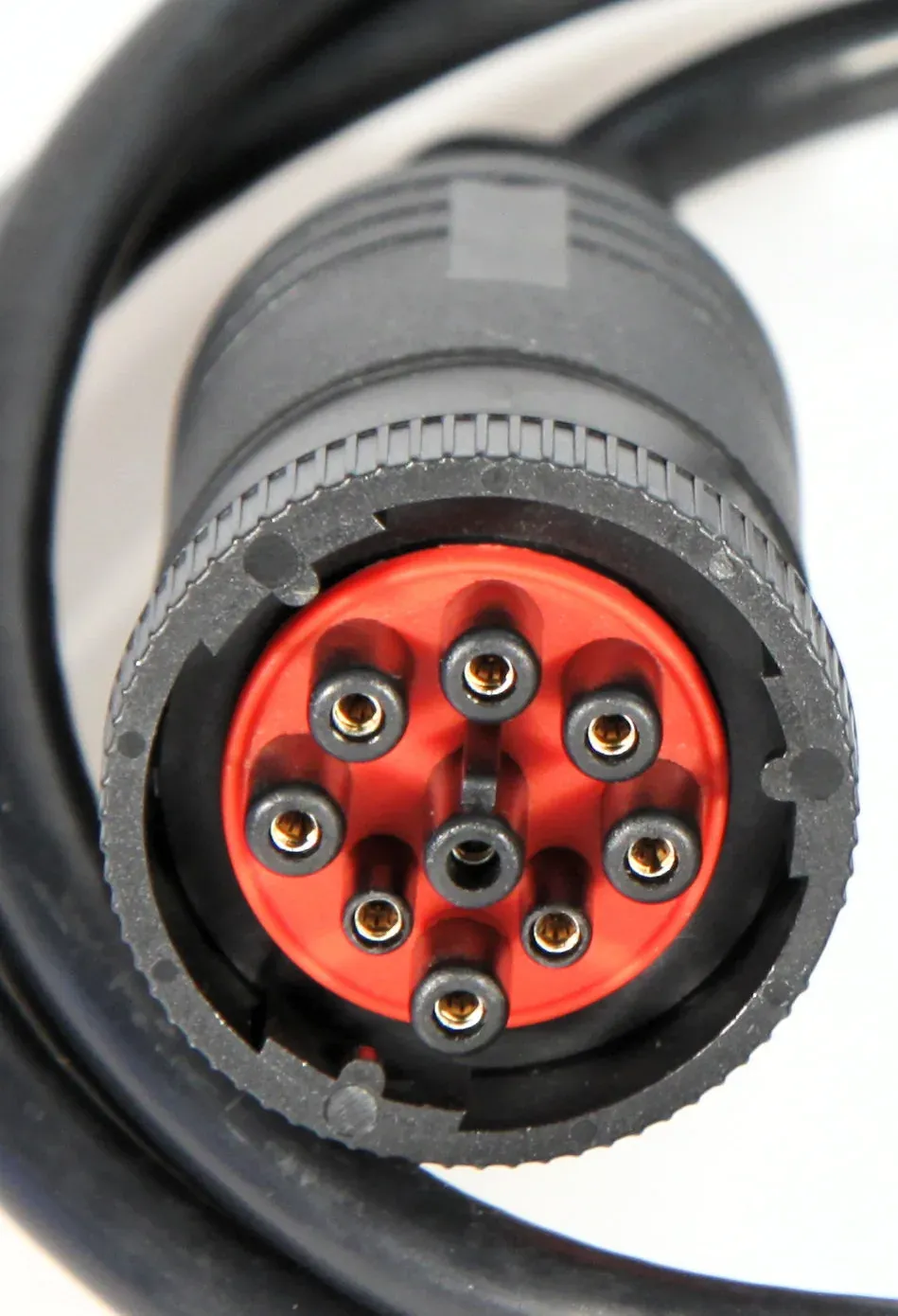 A close-up of a black, threaded, cylindrical electrical connector plug with nine gold pins set into a red insert, attached to a thick coiled cable.