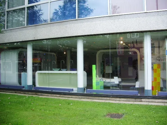 The glass-fronted ground floor of a modernist building, its window display arranged with pale blue and lime-green moulded fixtures.