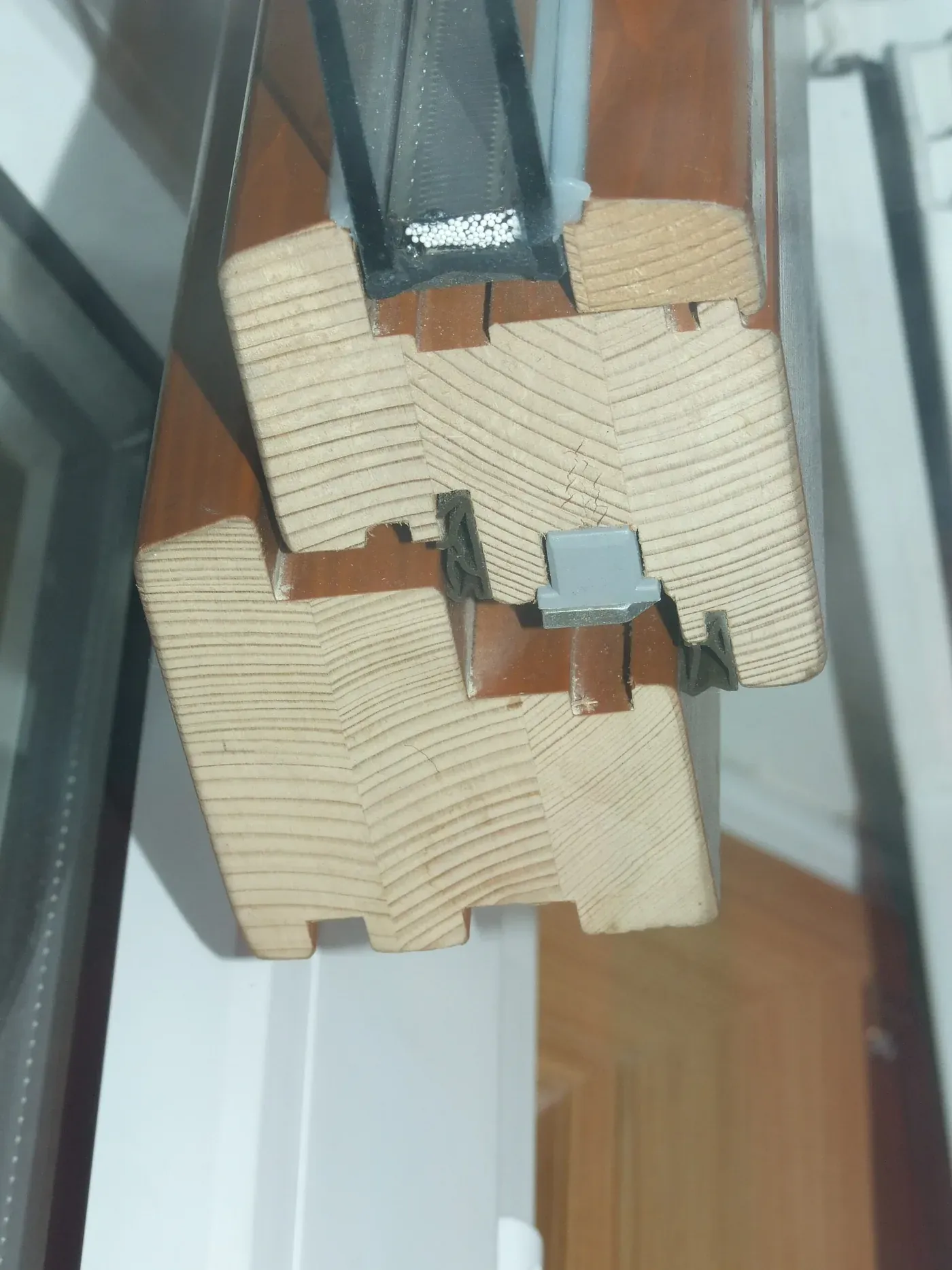 A cross-section of a wooden window frame showing a double-glazed unit, with a dark rubbery sealant strip visible in the channel between the two panes of glass.