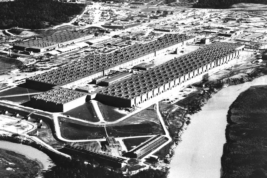 An aerial black-and-white photograph of the enormous U-shaped K-25 gaseous diffusion building at Oak Ridge, Tennessee, surrounded by smaller support buildings and roads.