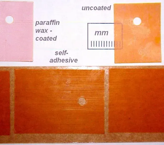 Four rectangular insulating pads laid out for comparison, one pink and three shades of amber-orange, each with a small mounting hole punched through the centre and hand-written labels identifying coating types beside them.