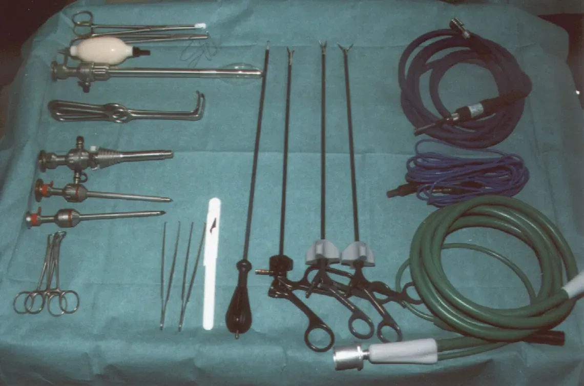 An overhead photograph of surgical instruments laid out on green cloth, including several long, thin metal rods with pistol-grip handles, trocar sheaths, curved forceps, and coiled cables for light and insufflation.