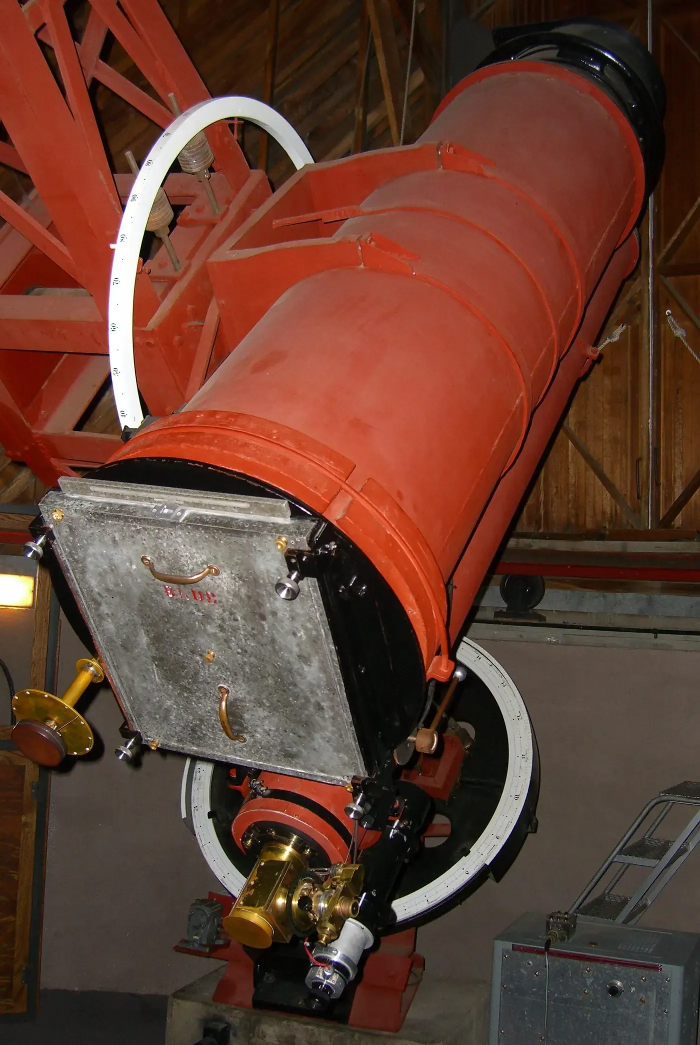 A large red-painted telescope tube mounted on a heavy pier inside a wooden observatory dome, angled steeply upward.