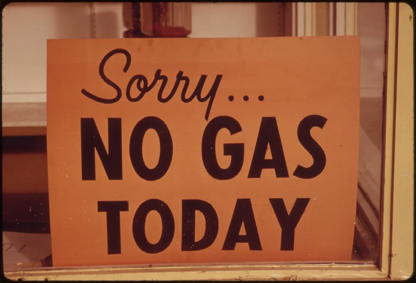 A hand-lettered orange sign reading Sorry... No Gas Today, propped in the window of a filling station.