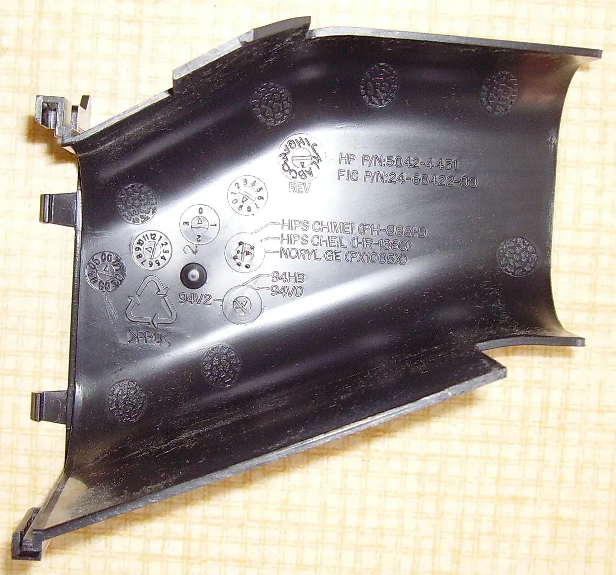 The underside of a black molded plastic computer duct, stamped with manufacturer part numbers, resin-identification codes, and the text NORYL GE PX1005X beside a PPO recycling symbol.