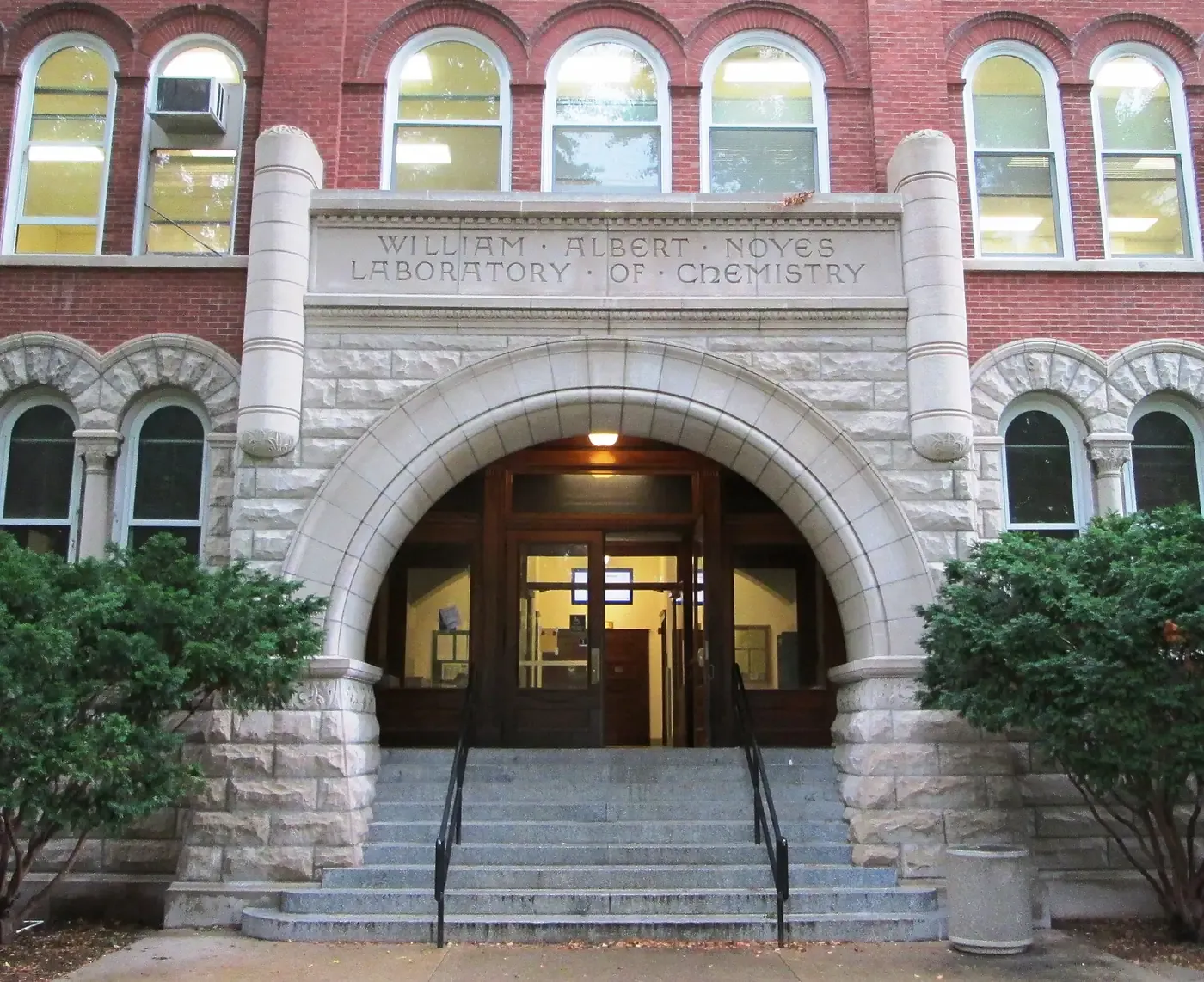 The stone-arched entrance of a red-brick university building, its lintel carved WILLIAM ALBERT NOYES LABORATORY OF CHEMISTRY, flanked by trimmed shrubs and a short flight of steps.