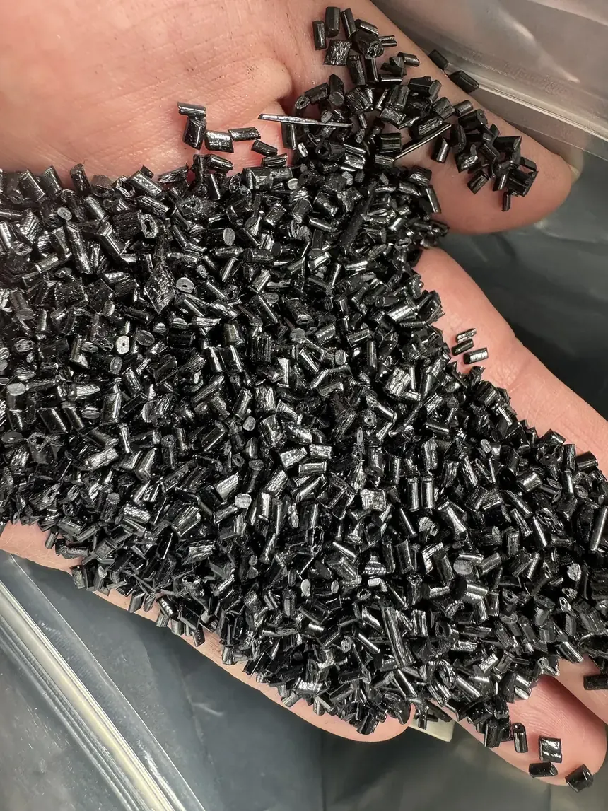 A close-up photograph of a person's cupped hand holding a large quantity of small black cylindrical plastic pellets.