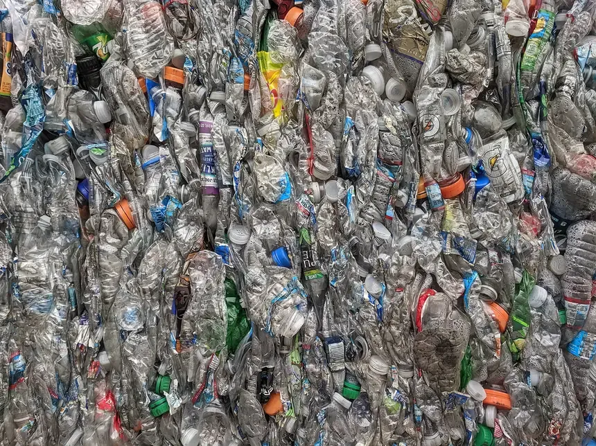 A tightly compressed bale of crushed, multicoloured PET bottles and caps, viewed close up, at a recycling facility.