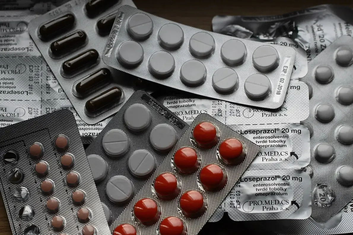 Several silver foil-backed pharmaceutical blister packs containing round tablets and dark oblong capsules, photographed close together on a wooden surface.