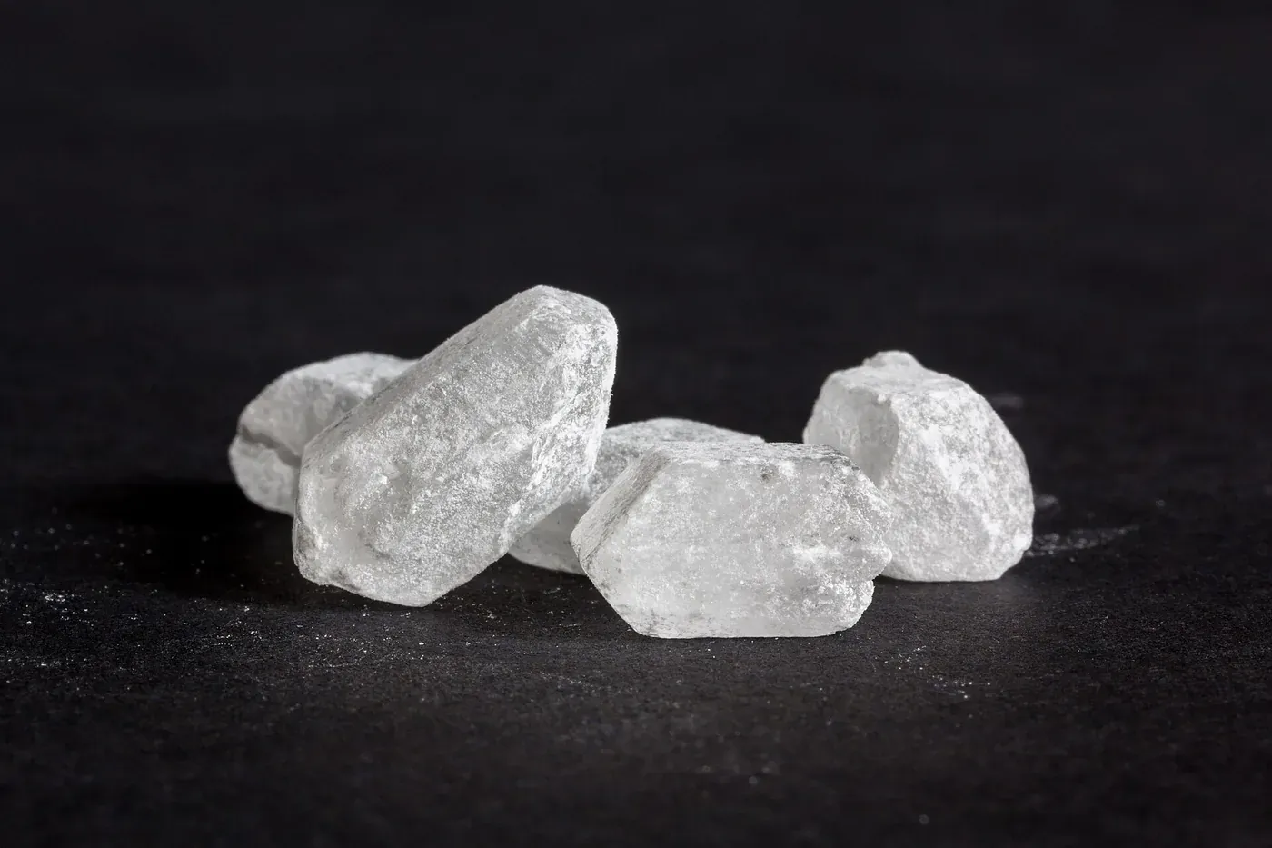 Several large, irregular, translucent white crystals of rock candy sugar resting on a dark surface.
