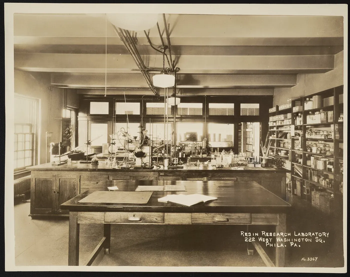 A wood-panelled chemistry laboratory with long benches crowded with glassware and distillation apparatus, and shelves of labelled reagent bottles along one wall.