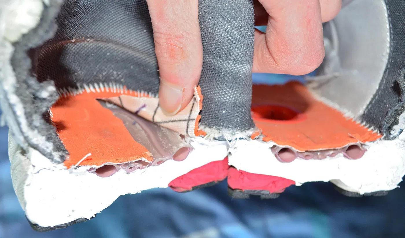 Close-up of a cut-open running shoe, showing layers of white foam, orange fabric and small internal air pockets inside the sole.