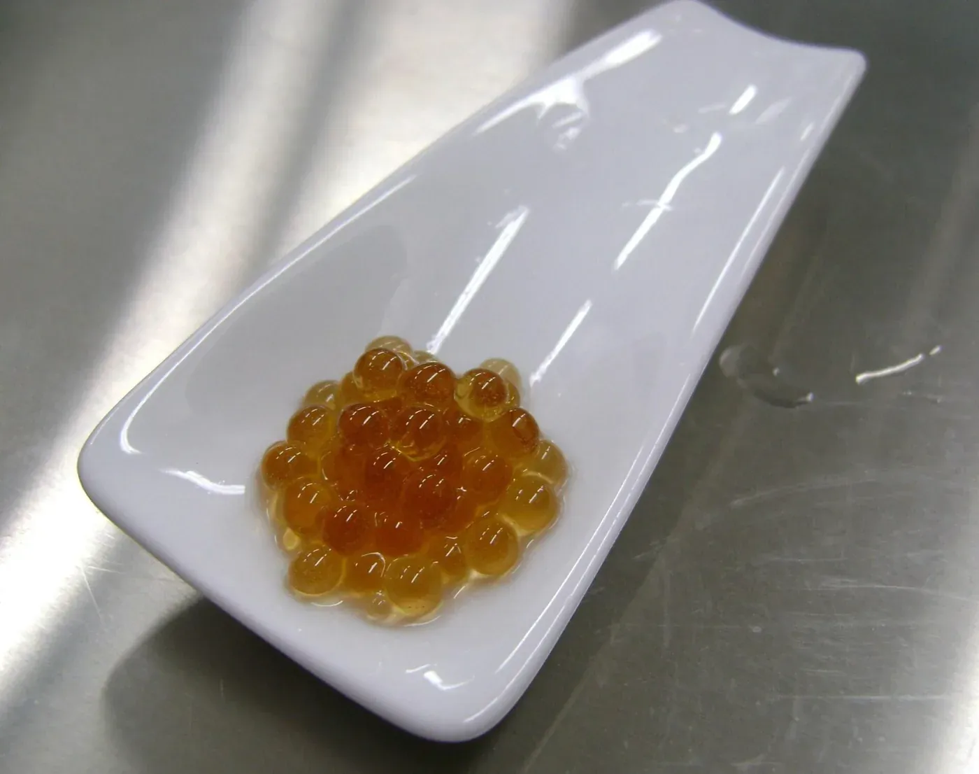 A small white ceramic plate holding a cluster of glistening amber spheres, each about the size of a large pearl, in a light syrup.